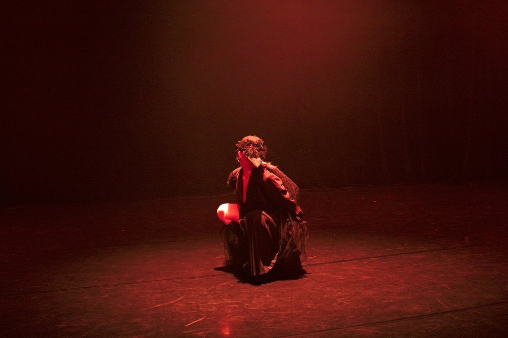 eine Person sitzt im roten Licht da und trägt eine bunte Krähenmaske