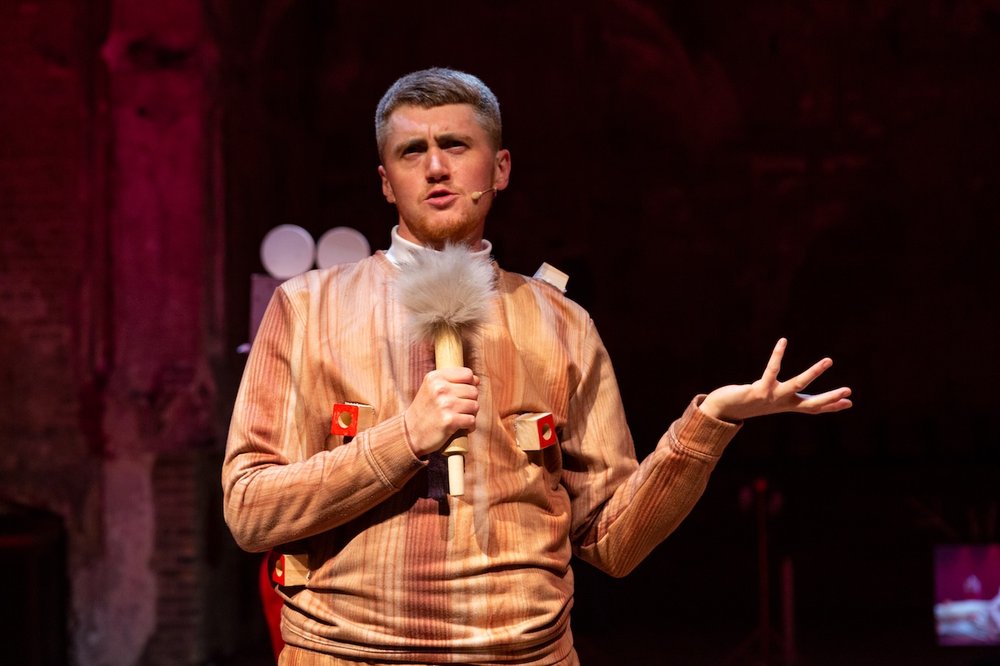 Ivor MacAskill spricht in eine Mikrofon mit Puschel und hält die linke Hand erklärend hoch. Ivor hat kurze Haare und einen leichten Schnäuzer.