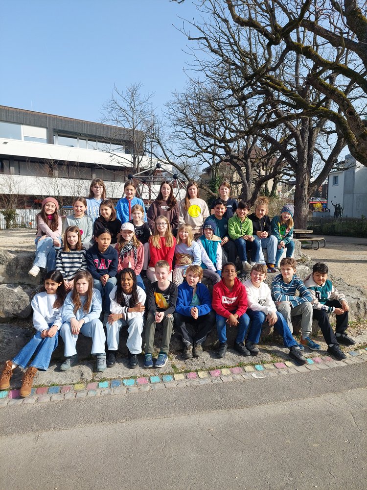 in drei Reihen voreinander sind die Schüler*innen der Primarschule vor ihrem Schulhaus. Die Sonne scheint.