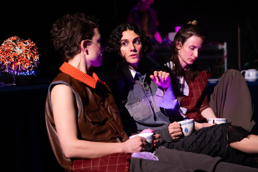 Drei Personen sitzen nebeneinander auf der Bühne und unterhalten sich, sie hören einander konzentriert zu.